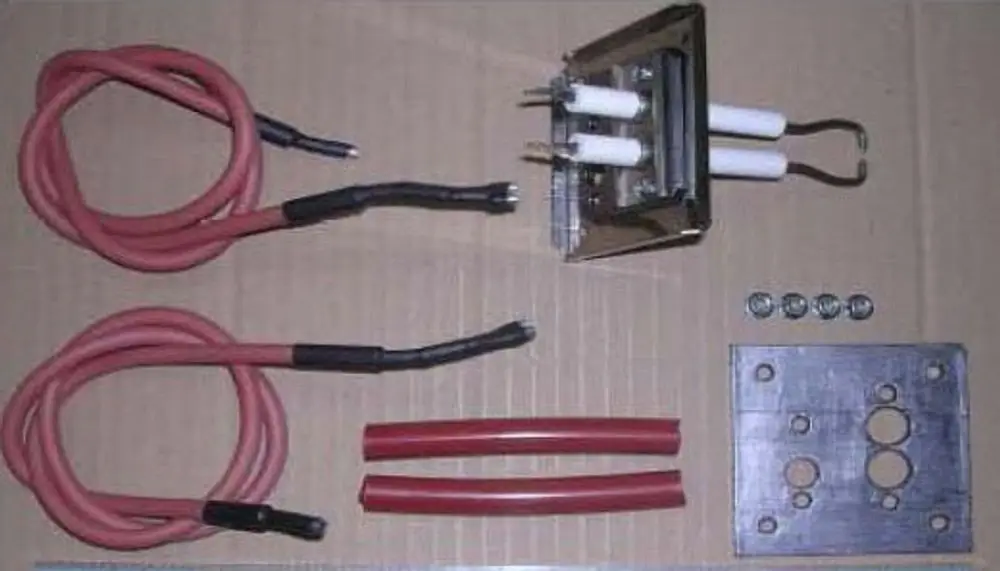 Zündeinheit von Remeha mit zwei elektrischen Zündkerzen, Kabeln, Schrauben und einer Metallplatte. Komponenten sind auf einem Karton angeordnet.